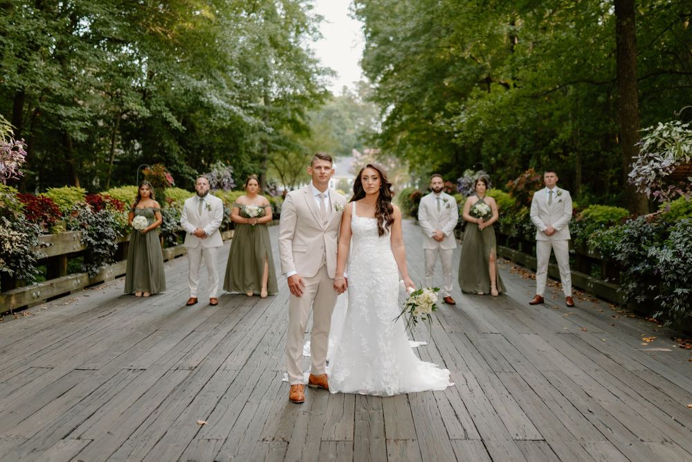 Wedding party posed for formal photos on a wooden deck surrounded by trees.