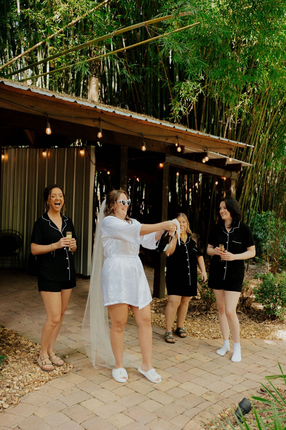 A group of dancers in black and white outfits perform a choreographed sequence on a paved pathway surrounded by bamboo.