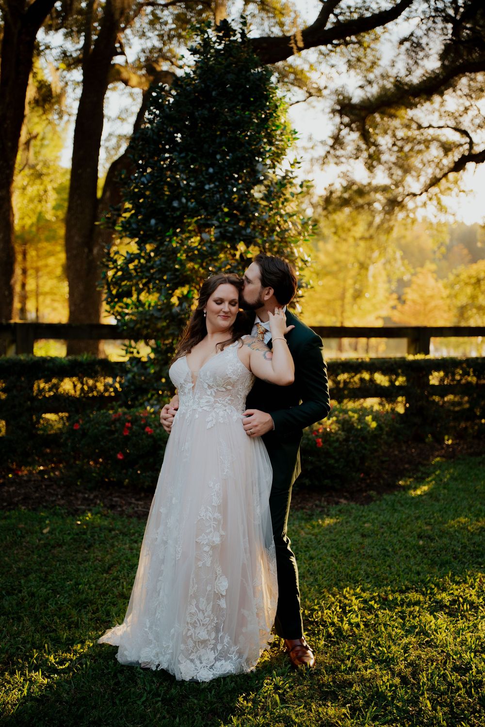A couple shares an intimate moment during sunset in a rustic outdoor setting with wooden fencing and golden light.