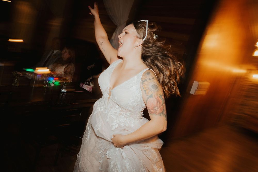 A couple in wedding attire dances together at a dimly lit reception venue with warm lighting and motion blur effects.