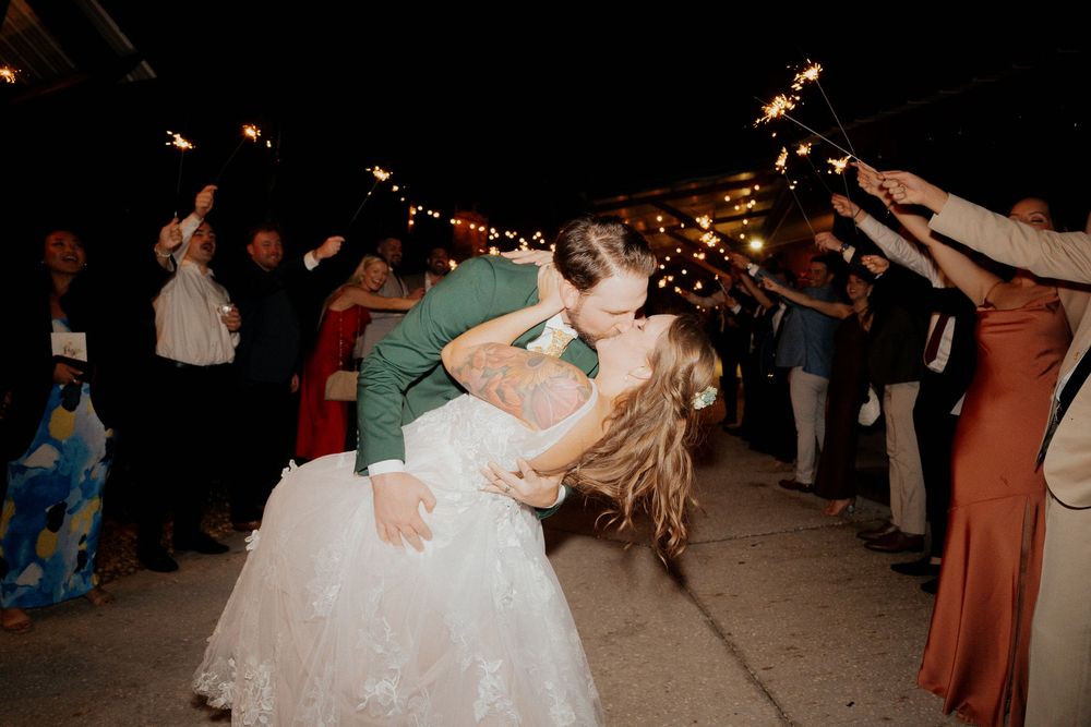 A couple shares a romantic dip during their first dance at a wedding reception while guests look on with sparklers.