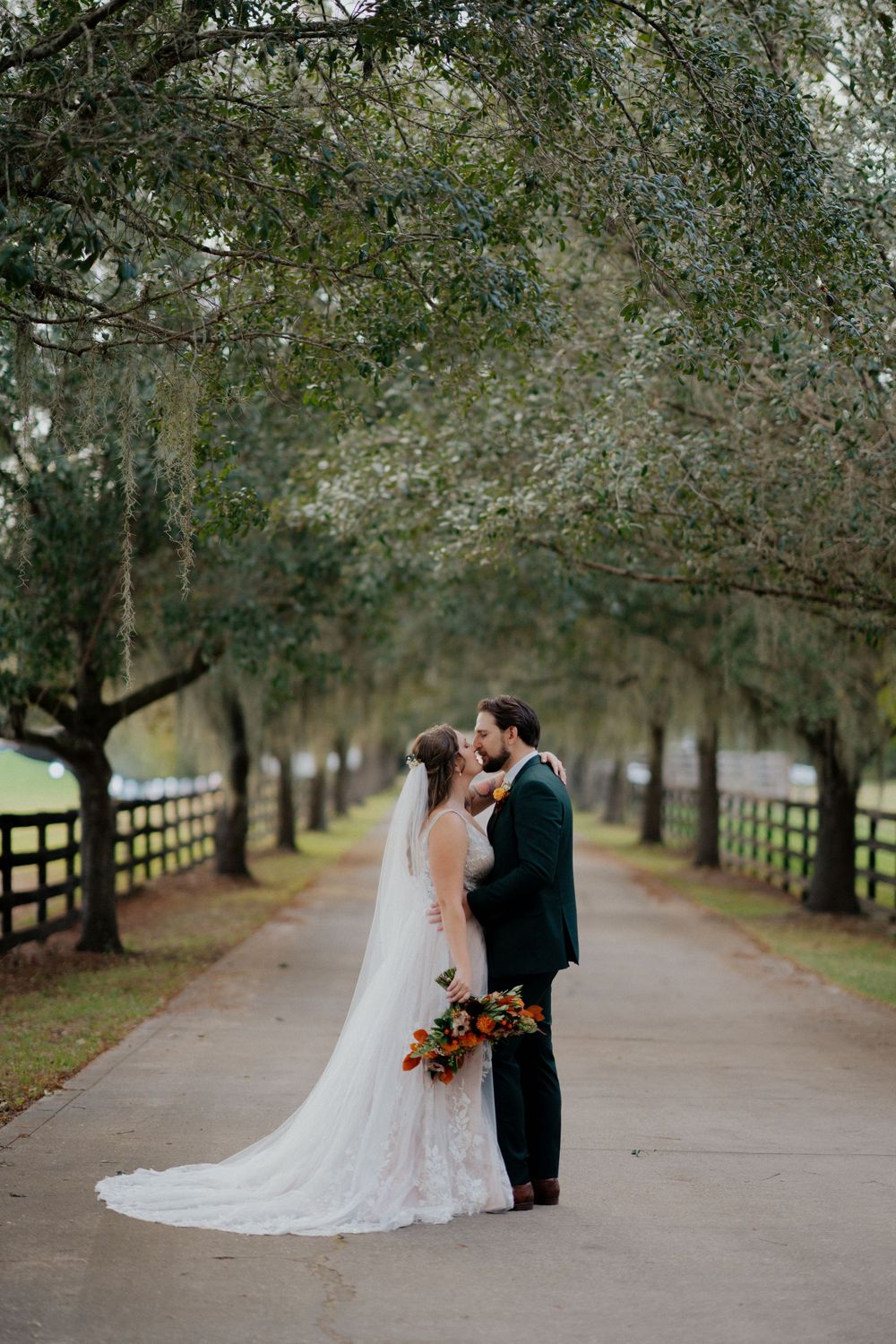 A romantic wedding couple shares intimate moments on a tree-lined path at club lake venue.