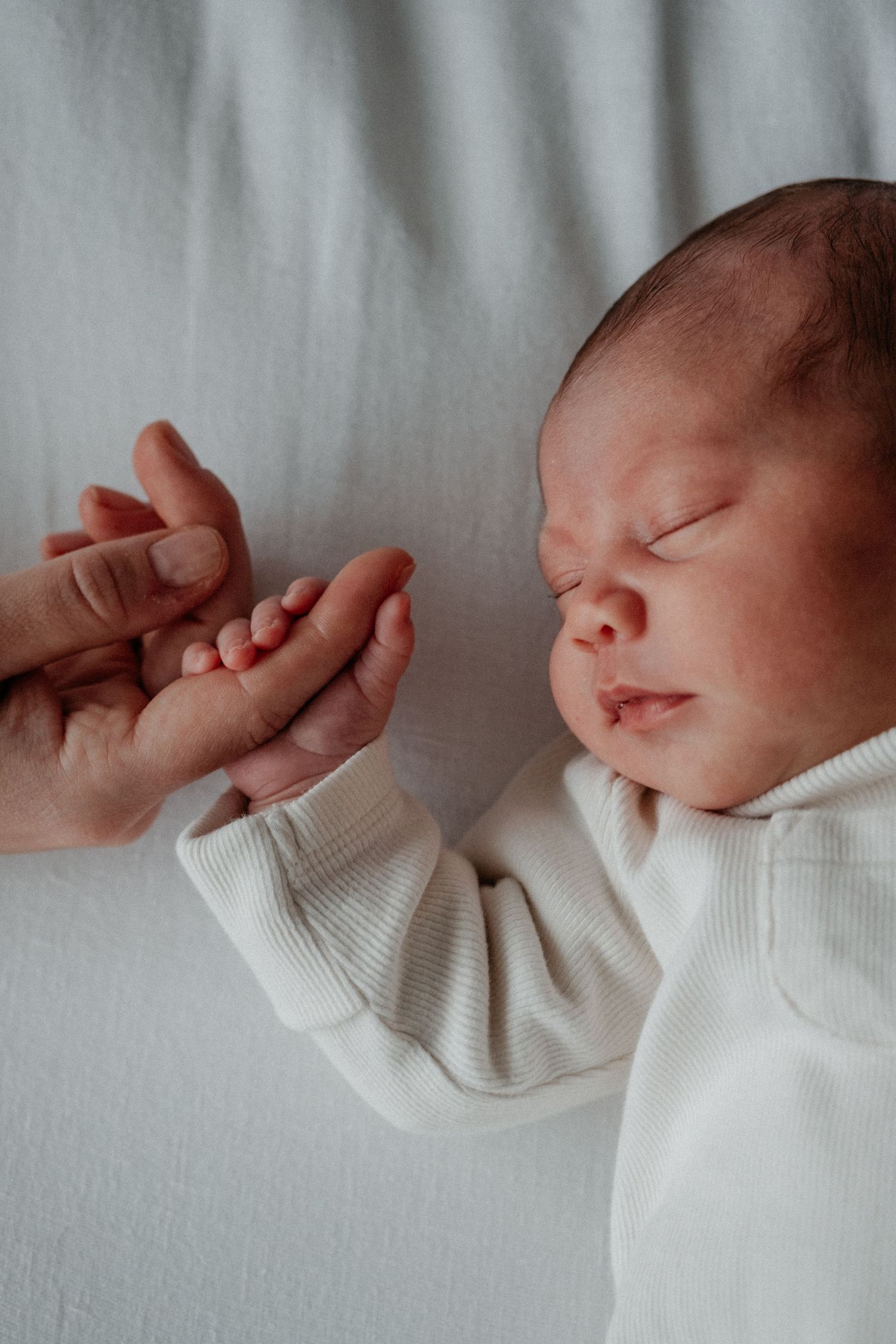 Close-up newborn portrait showing a baby holding a parent’s finger during a natural lifestyle newborn photography session.