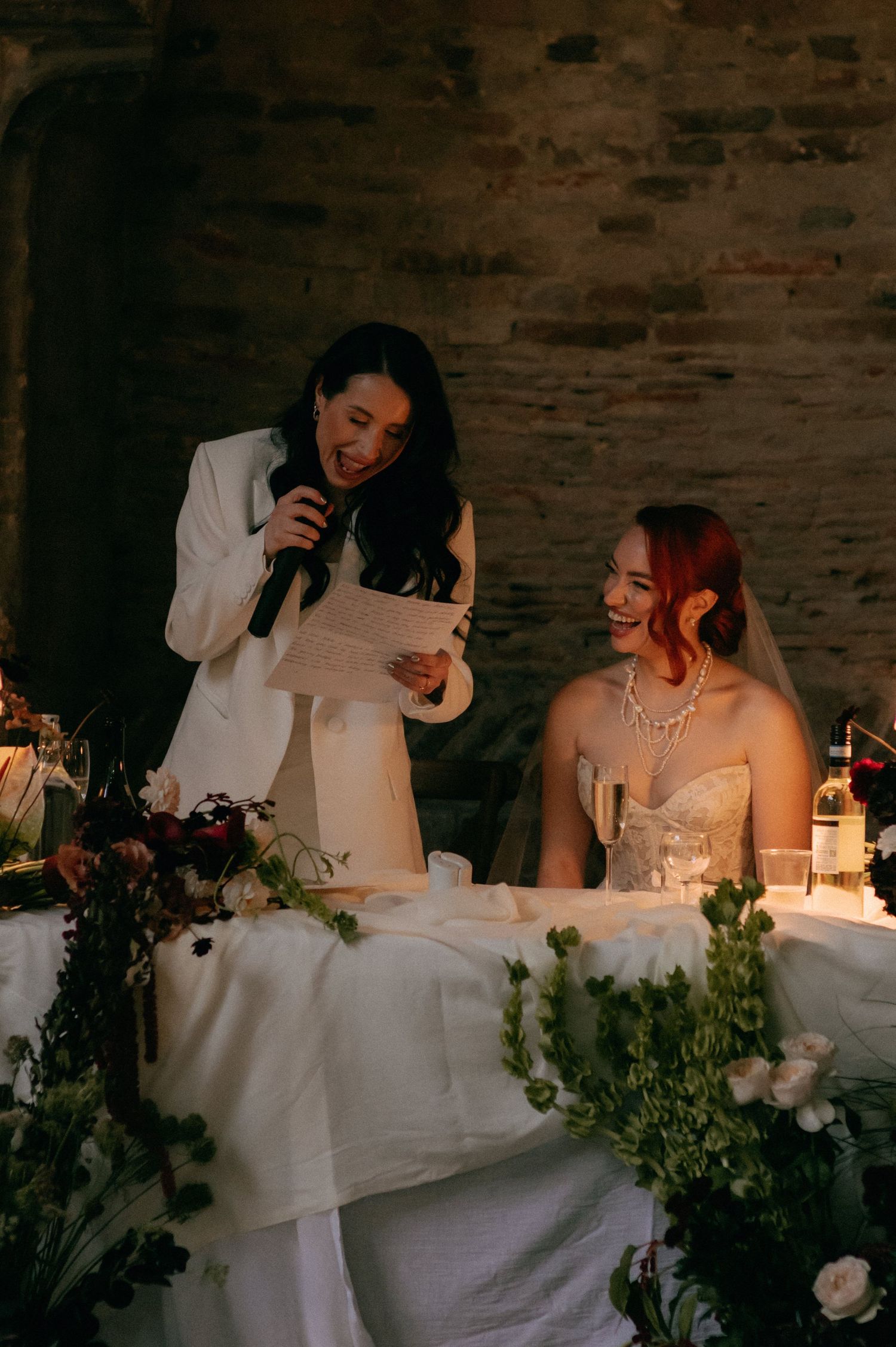 A candid wedding reception scene shows a couple seated at a table with white linens and greenery decorations.