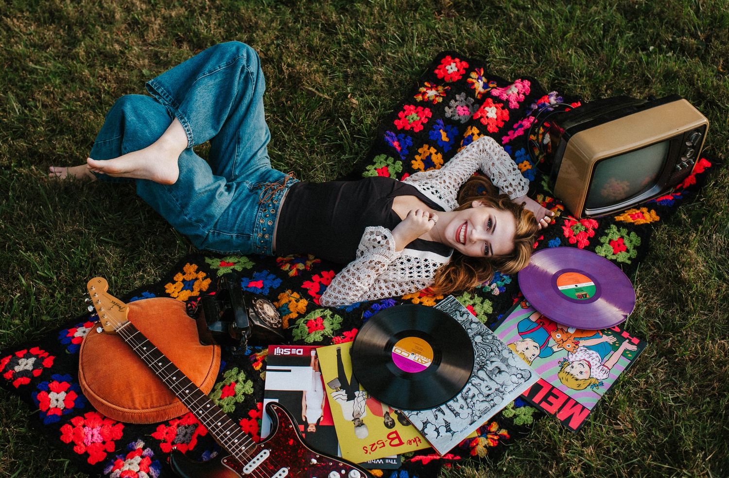 Vintage vinyl records and colorful retro items scattered on grass with polka dot pillows and nostalgic decor.