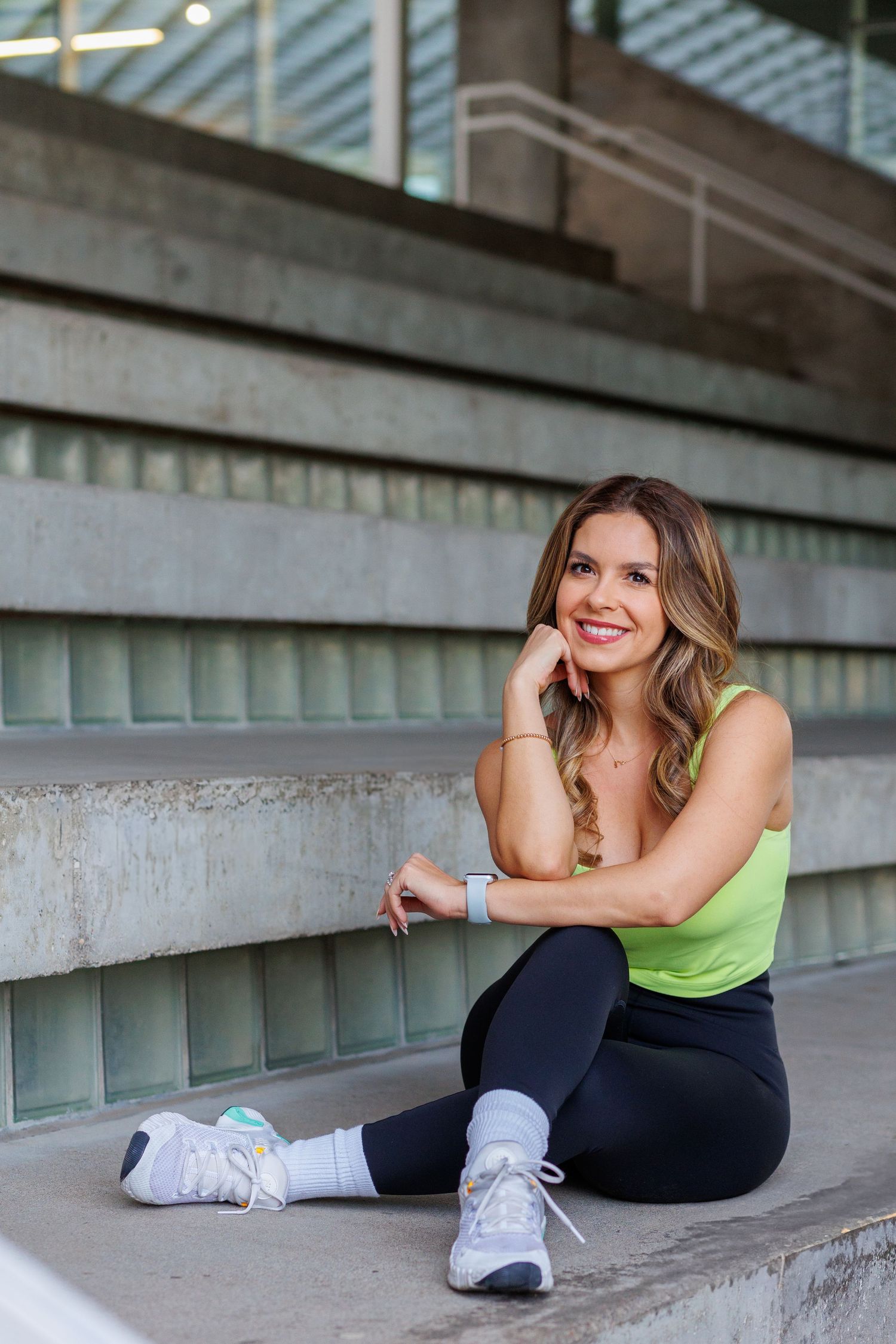 Happy athletic woman in green tank top and black leggings sitting on outdoor stadium steps smiling.