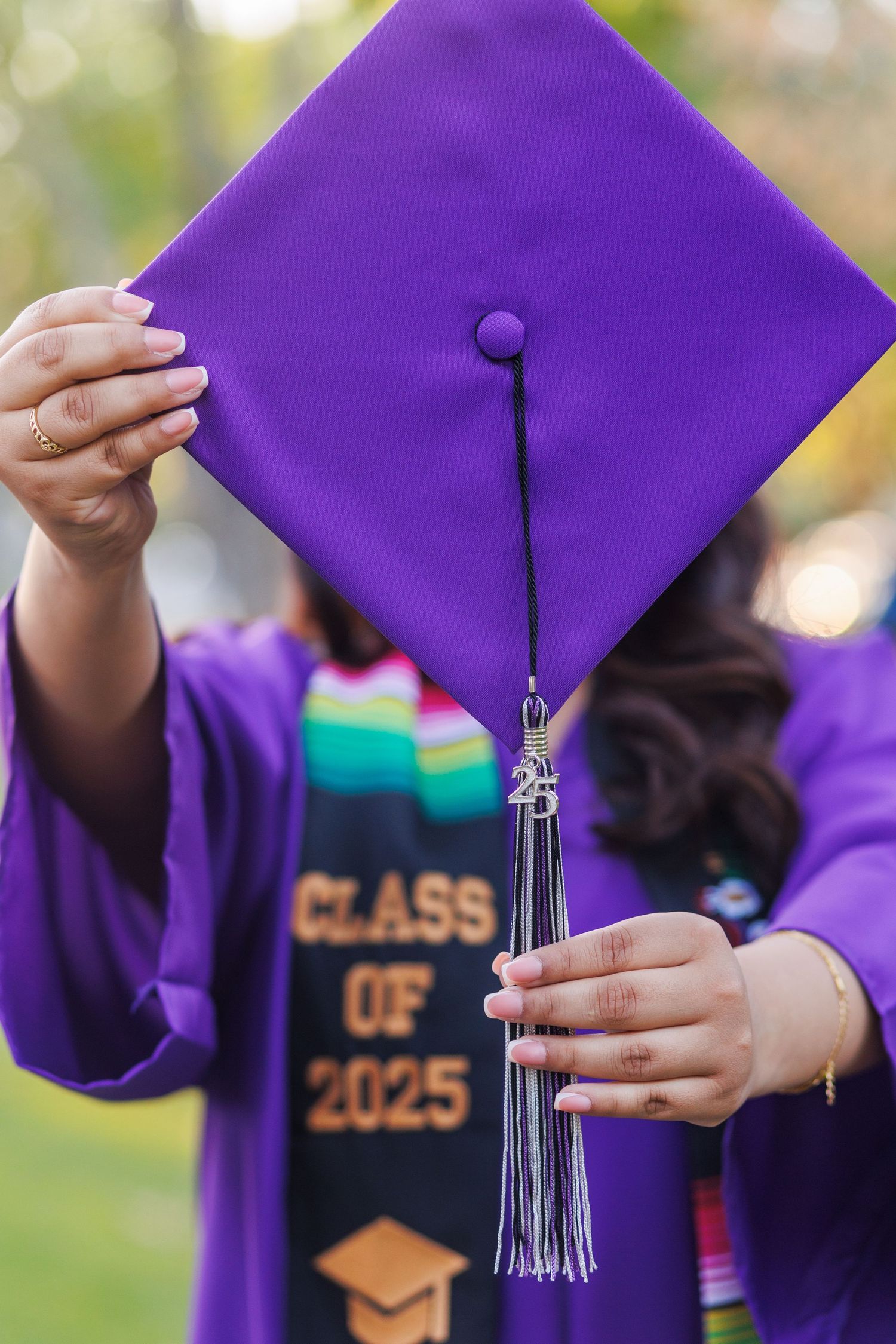 Close-up of hands holding purple graduation cap with Class of 2025 stole visible.