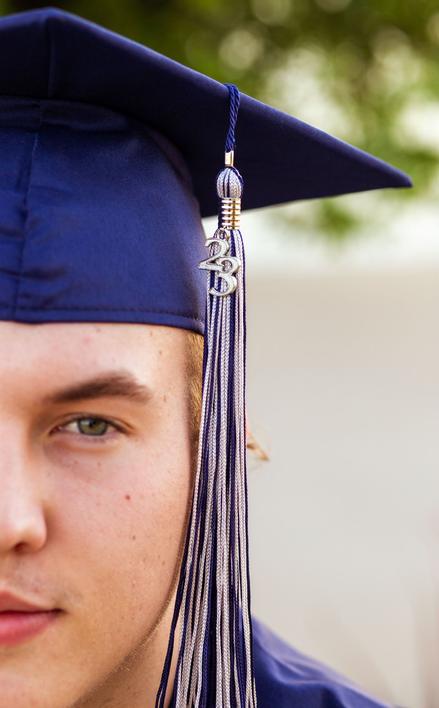 Close-up half portrait of young man wearing navy blue graduation cap with tassel.