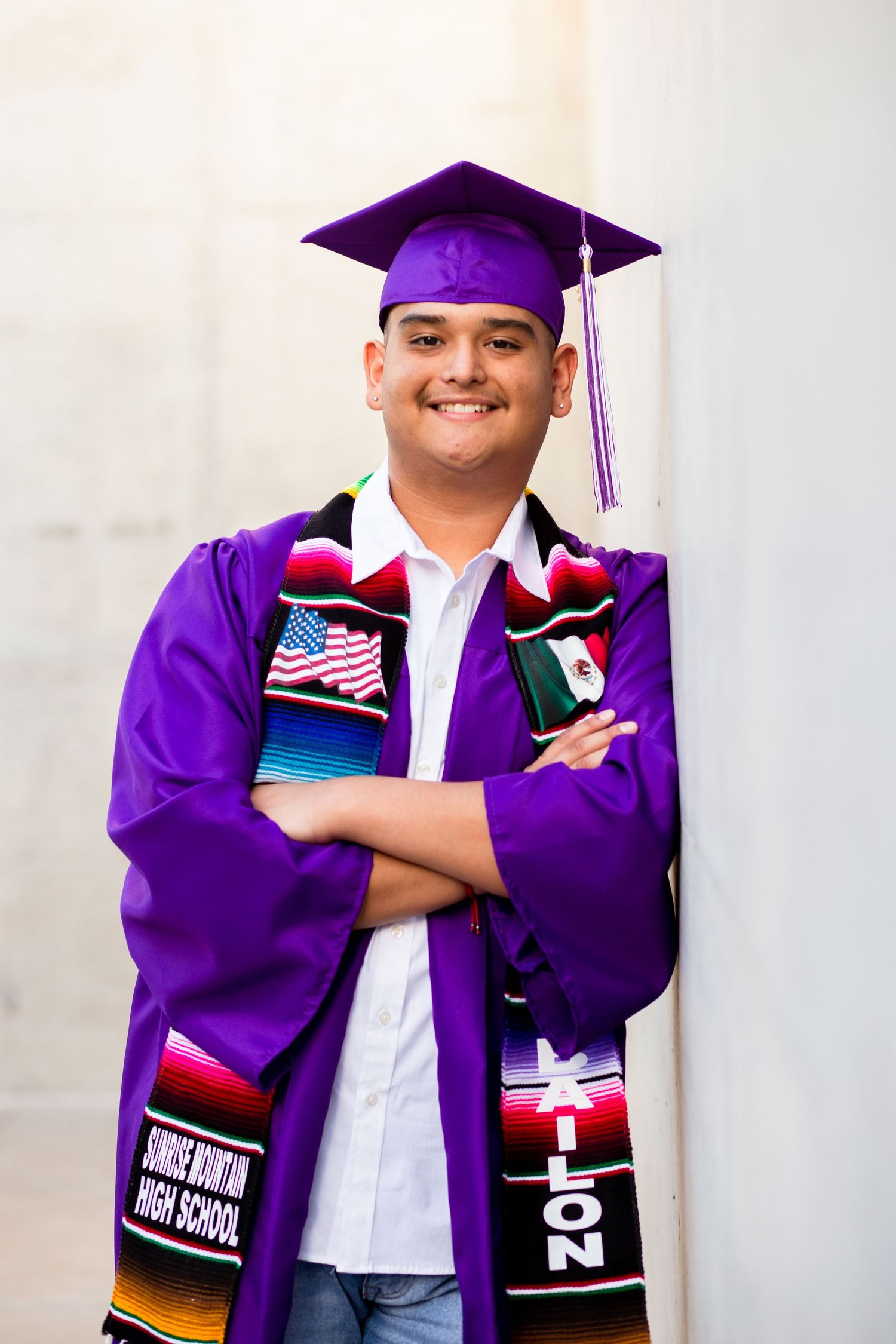 Smiling young male graduate in purple cap and gown with cultural graduation stole.