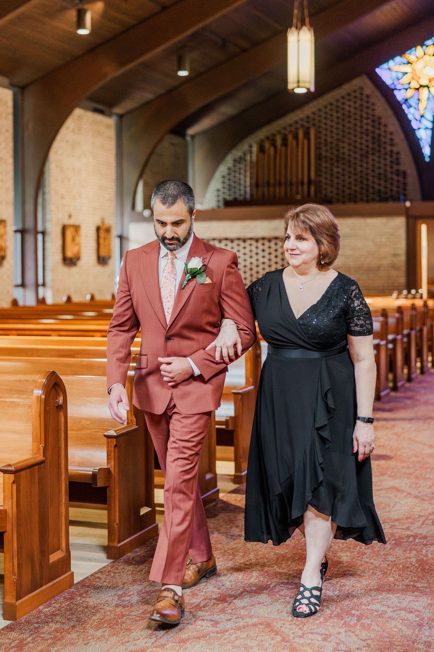 Couple walking through church aisle with rustic wooden pews and stained glass windows.