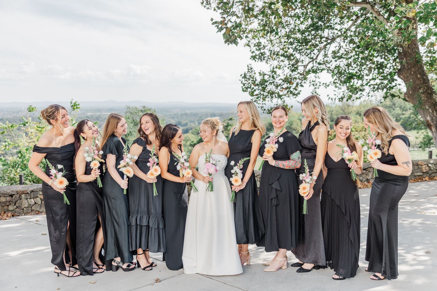 Wedding party members in black attire gathered for casual group photos under trees.