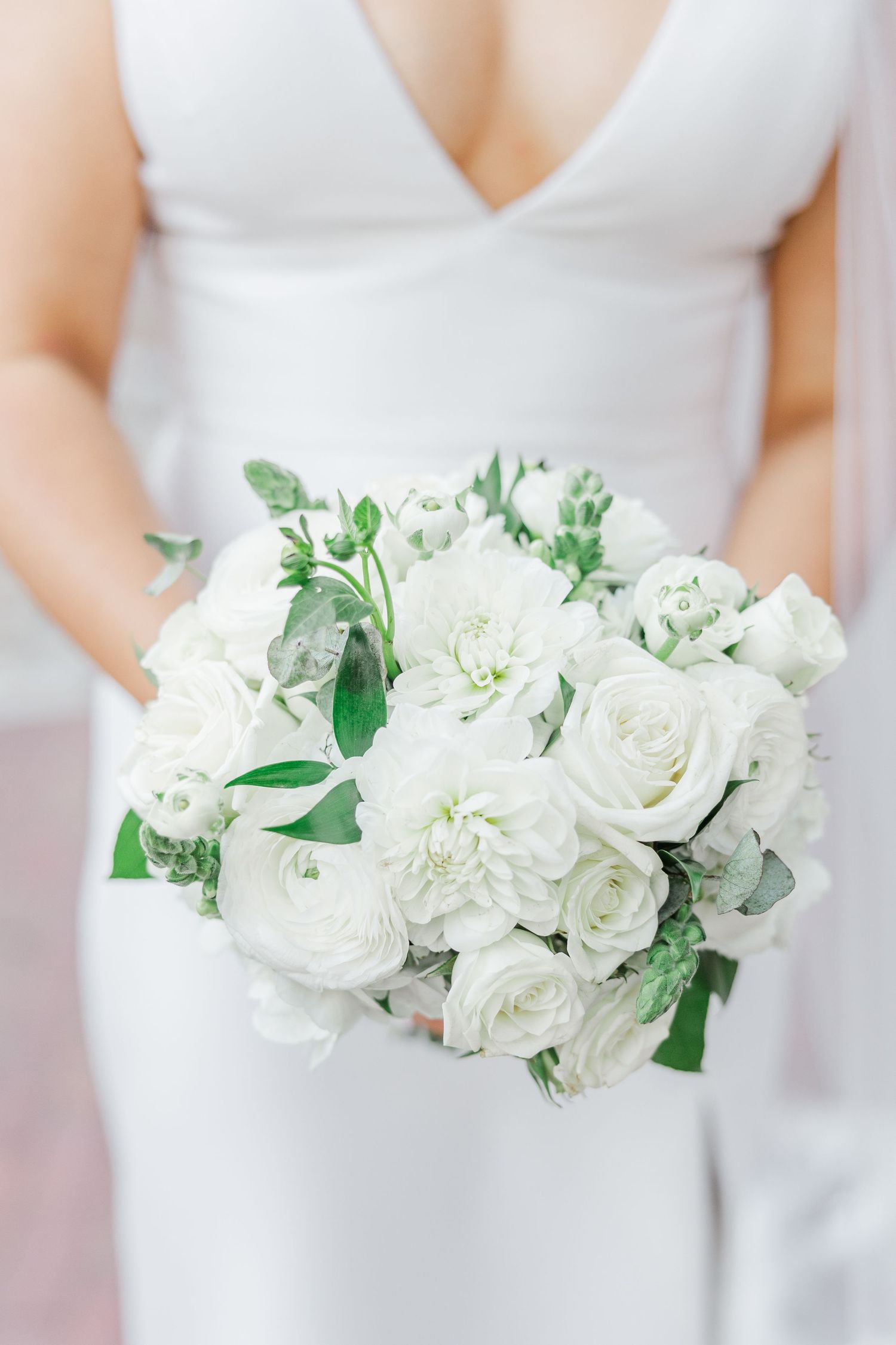 A series of elegant white bridal bouquets with roses and greenery held against white wedding dresses.