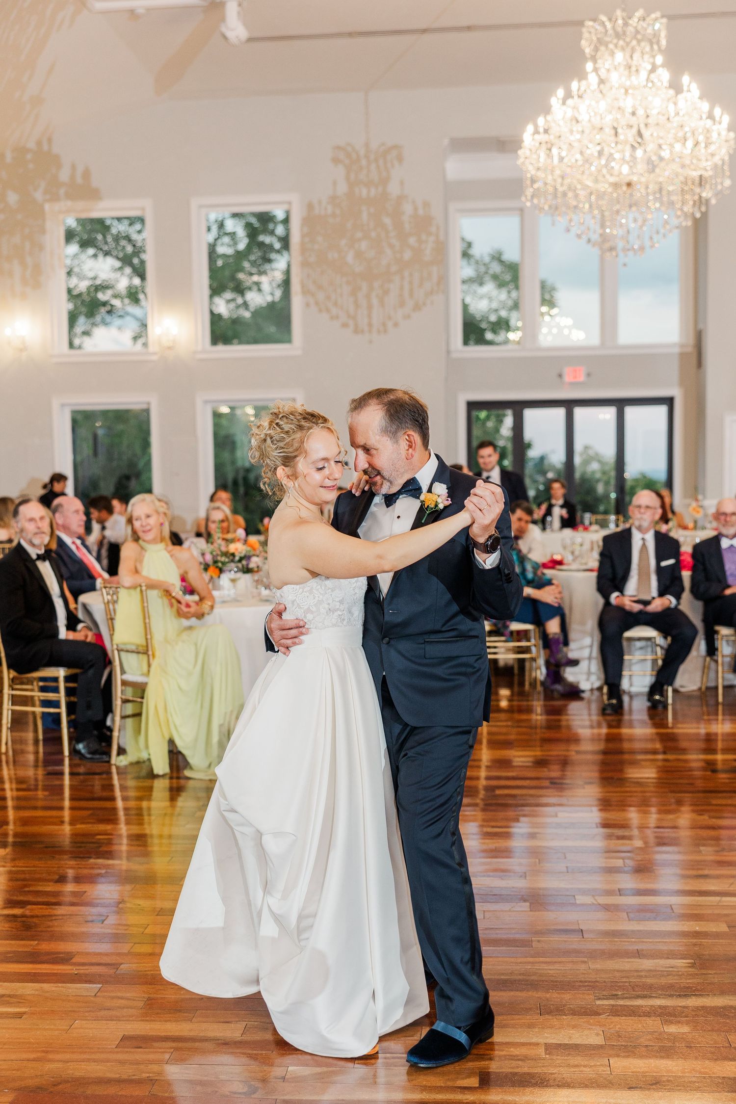 Wedding guests dance in an elegant ballroom with crystal chandeliers and hardwood floors during a reception celebration.