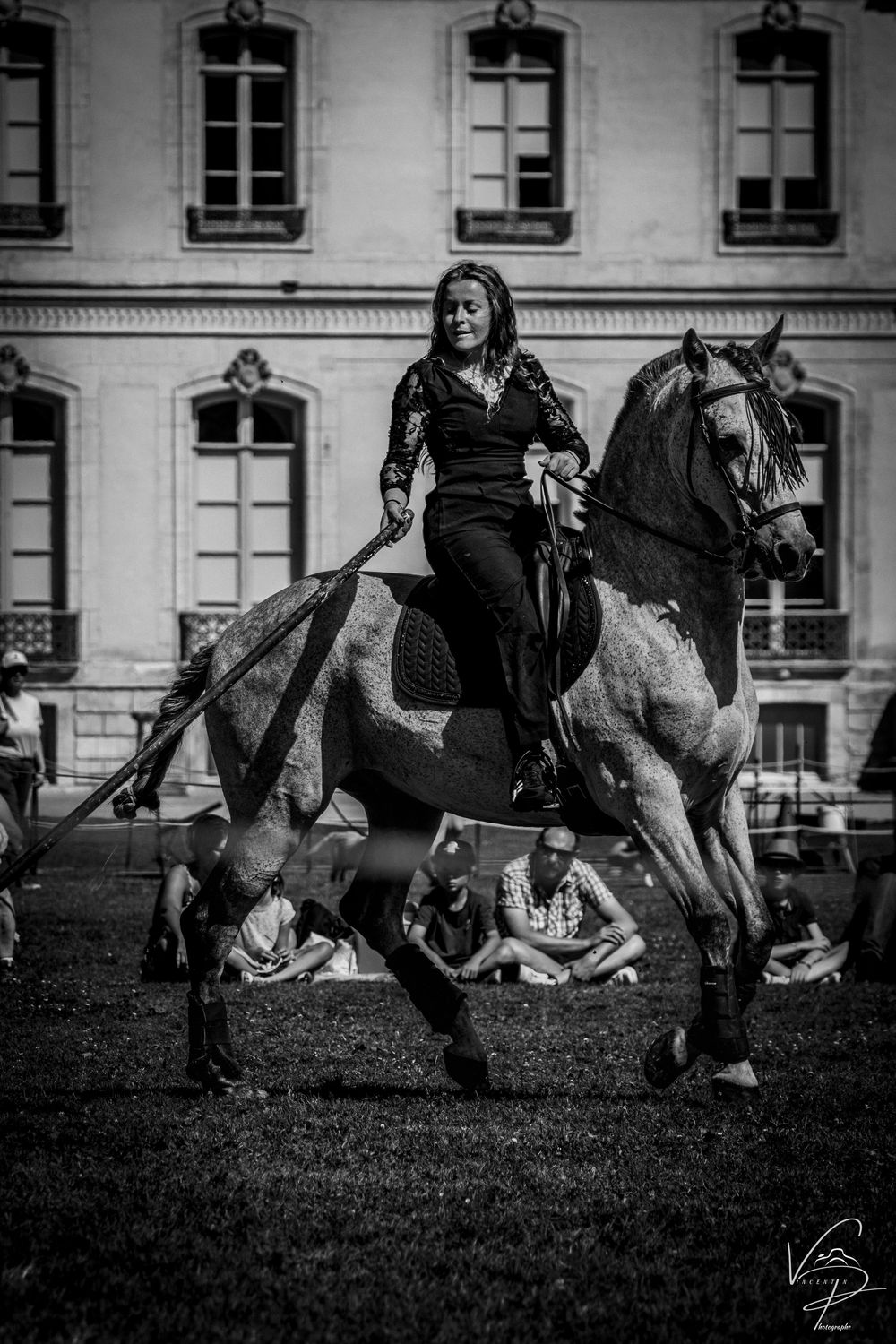 Black and white photo of a horse show performance with dramatic acrobatics against classic architecture.