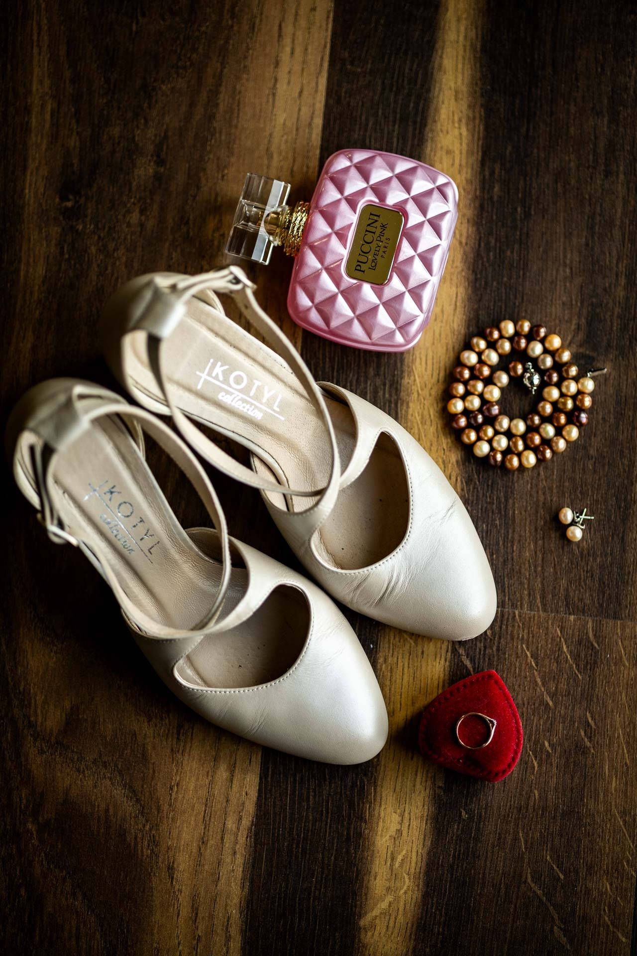 White bridal flats with pink quilted purse and pearl accessories on dark wooden floor.