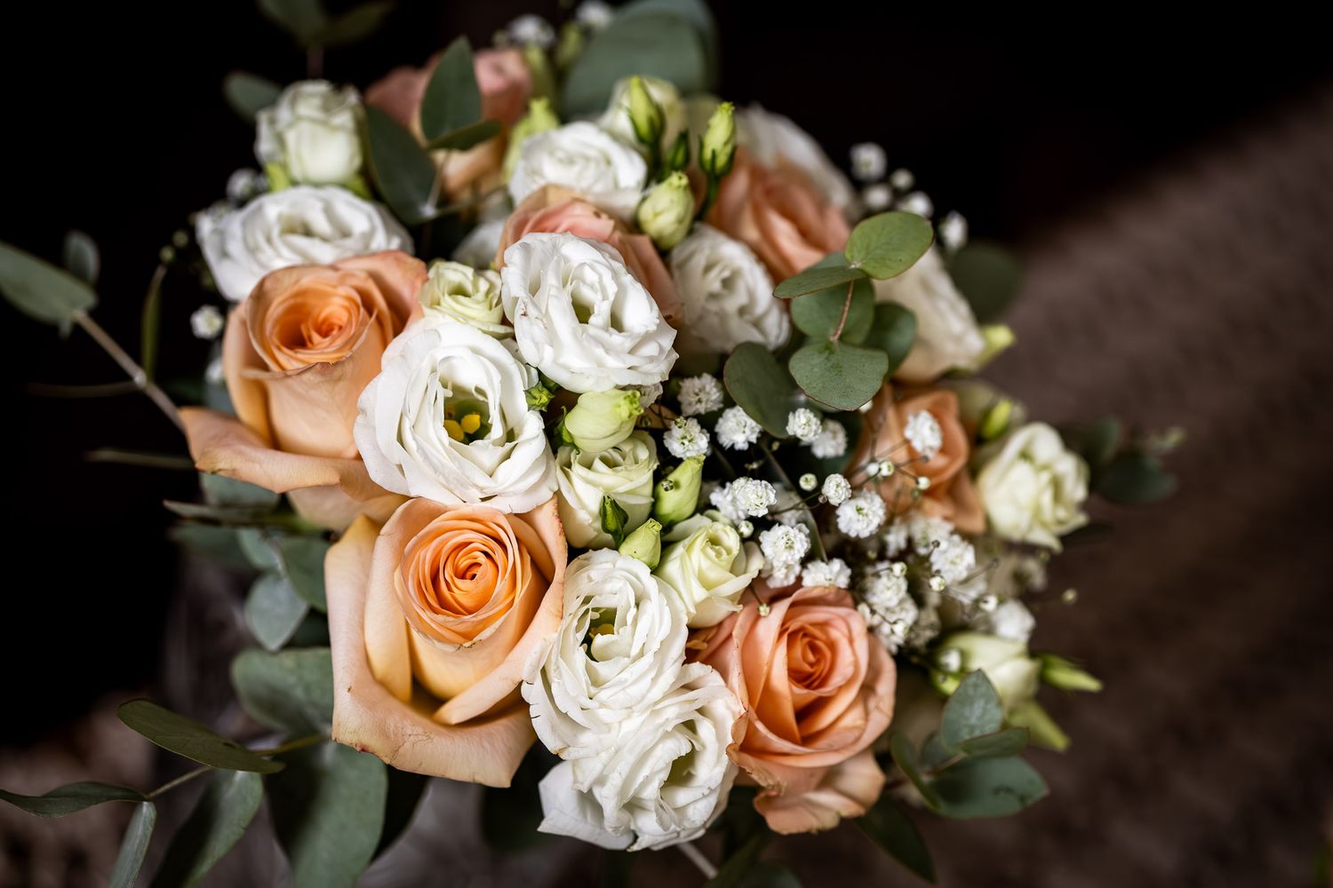 Peach roses and white floral wedding bouquet arrangement with greenery.