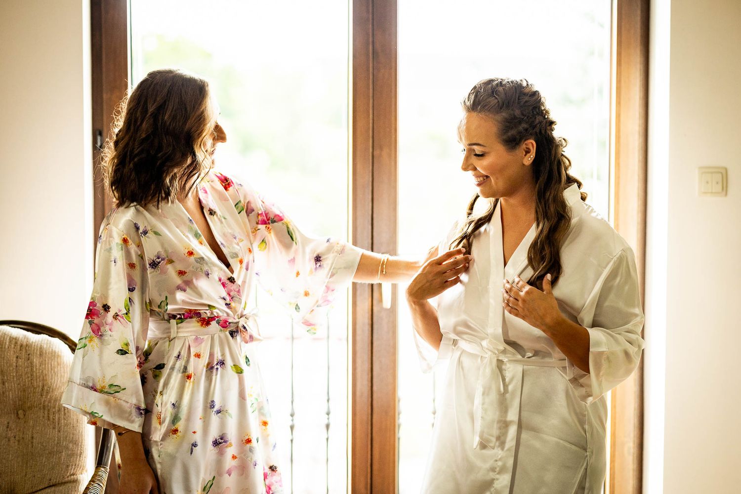 Two people having a quiet moment during wedding preparations in a sunlit room.