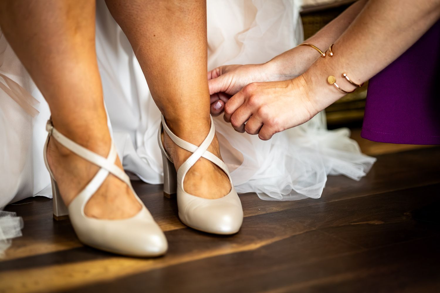 White ballet flats being secured on feet with tulle fabric in the background.