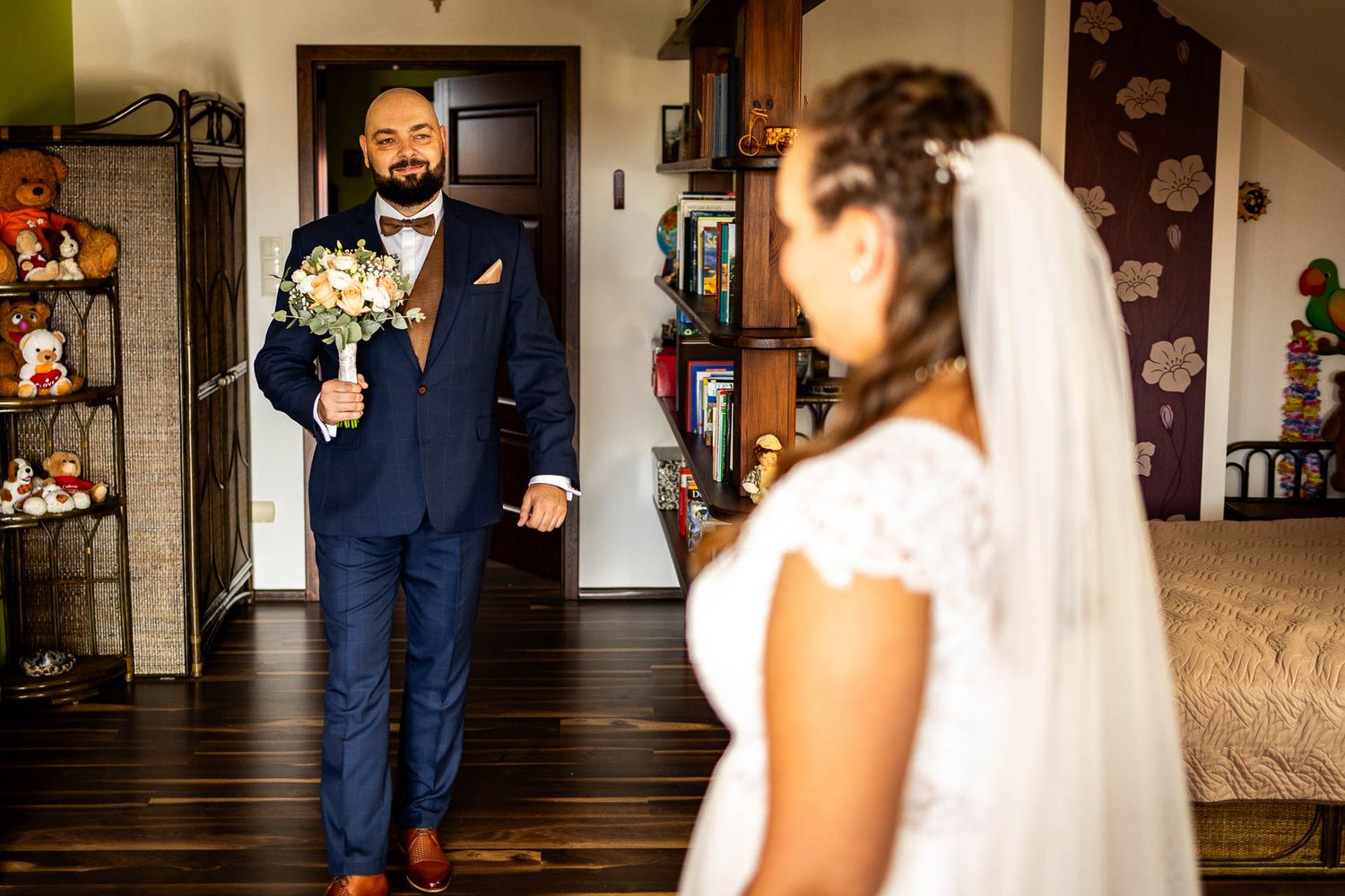 Wedding moment captured in a cozy room with dark floral wallpaper and wooden floors.