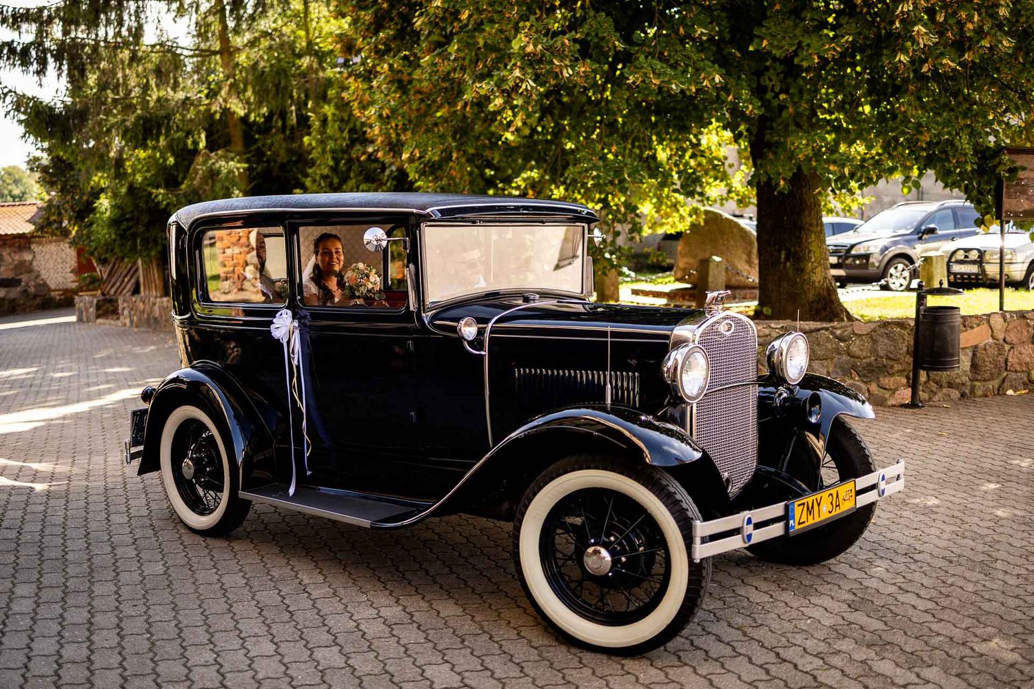 Classic vintage black car with white-wall tires parked on cobblestone street.