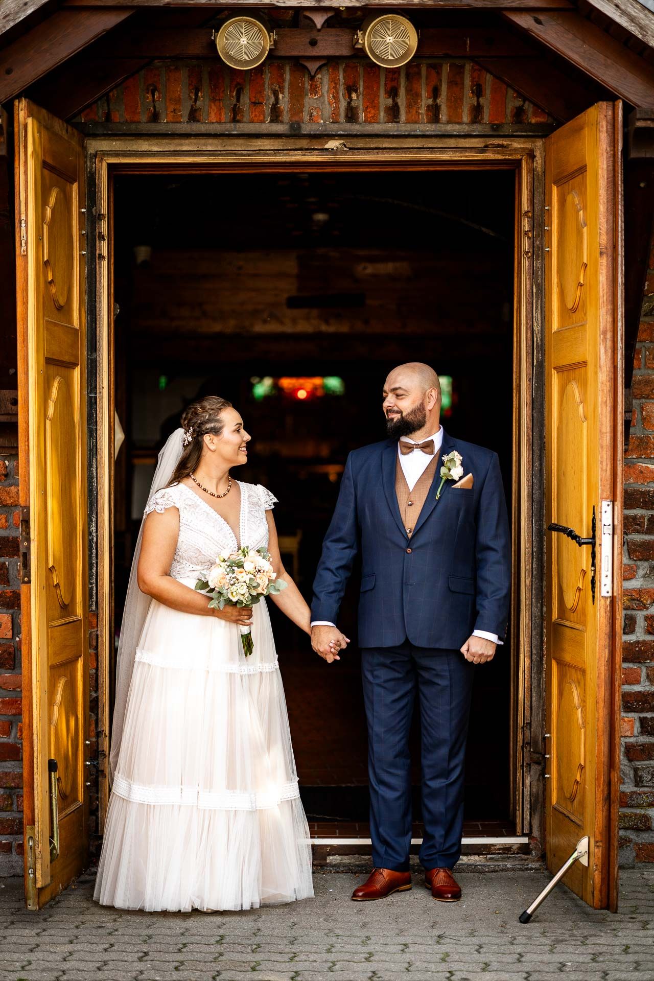 Wedding party posing under wooden beams in rustic venue.