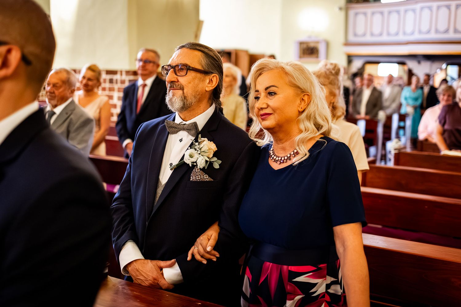 Wedding guests smile and watch the ceremony from wooden church pews.