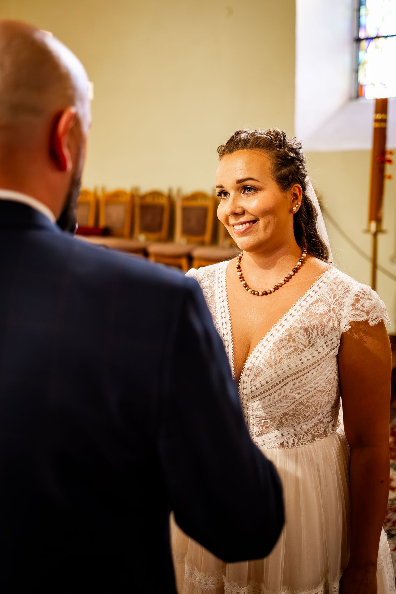 A bride in a beautiful white lace dress stands in a church interior.