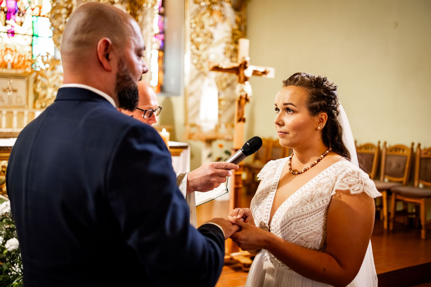 A couple exchanges vows during their wedding ceremony in a beautifully lit church.