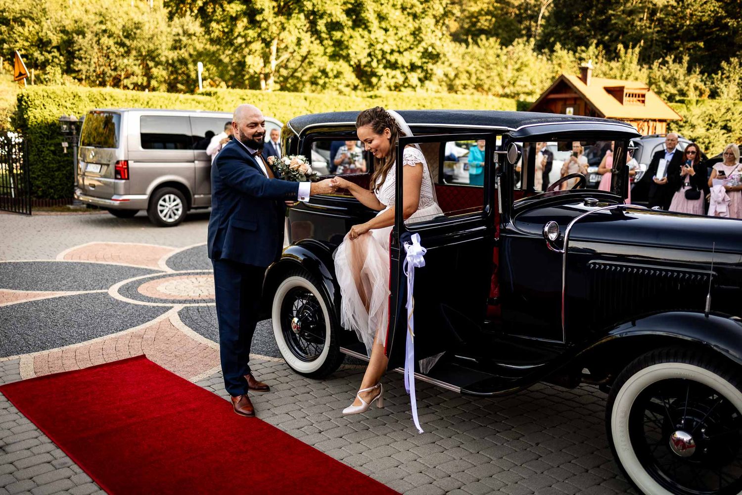 A classic vintage car with white wall tires serves as wedding transportation on a red carpet.