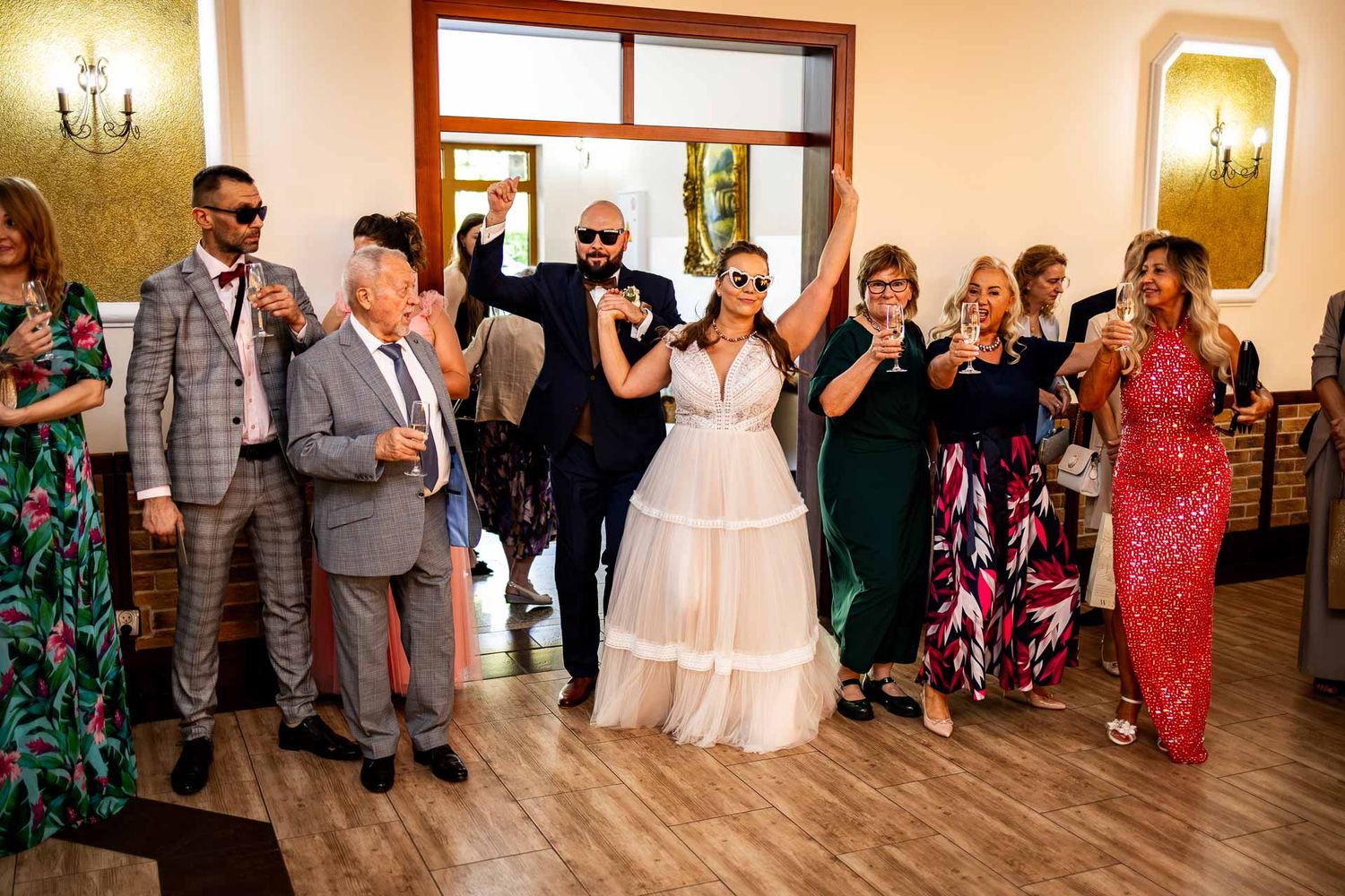 Wedding celebration with guests dancing on a wooden floor in colorful attire.