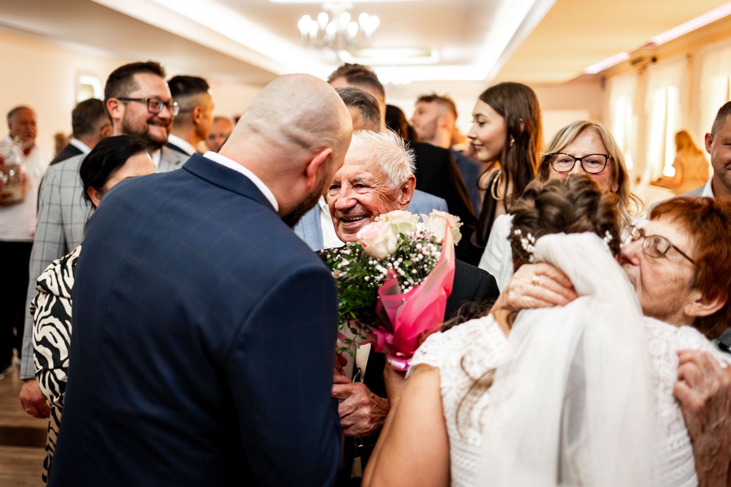 Wedding guests gather around to celebrate during an emotional reception moment.