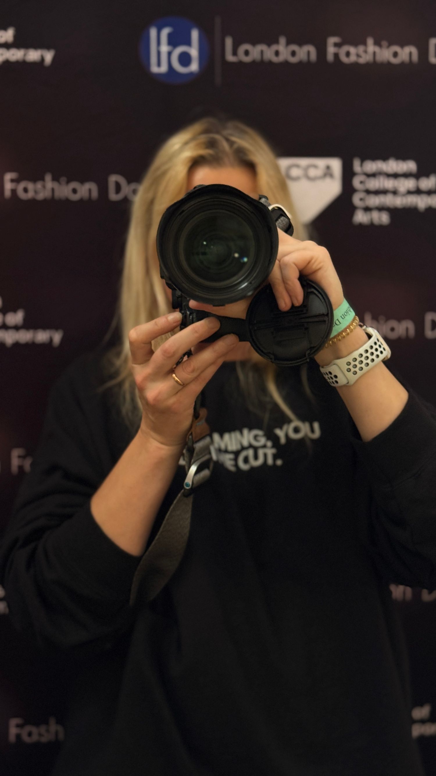 Photographer with camera against dark backdrop at London Fashion event.