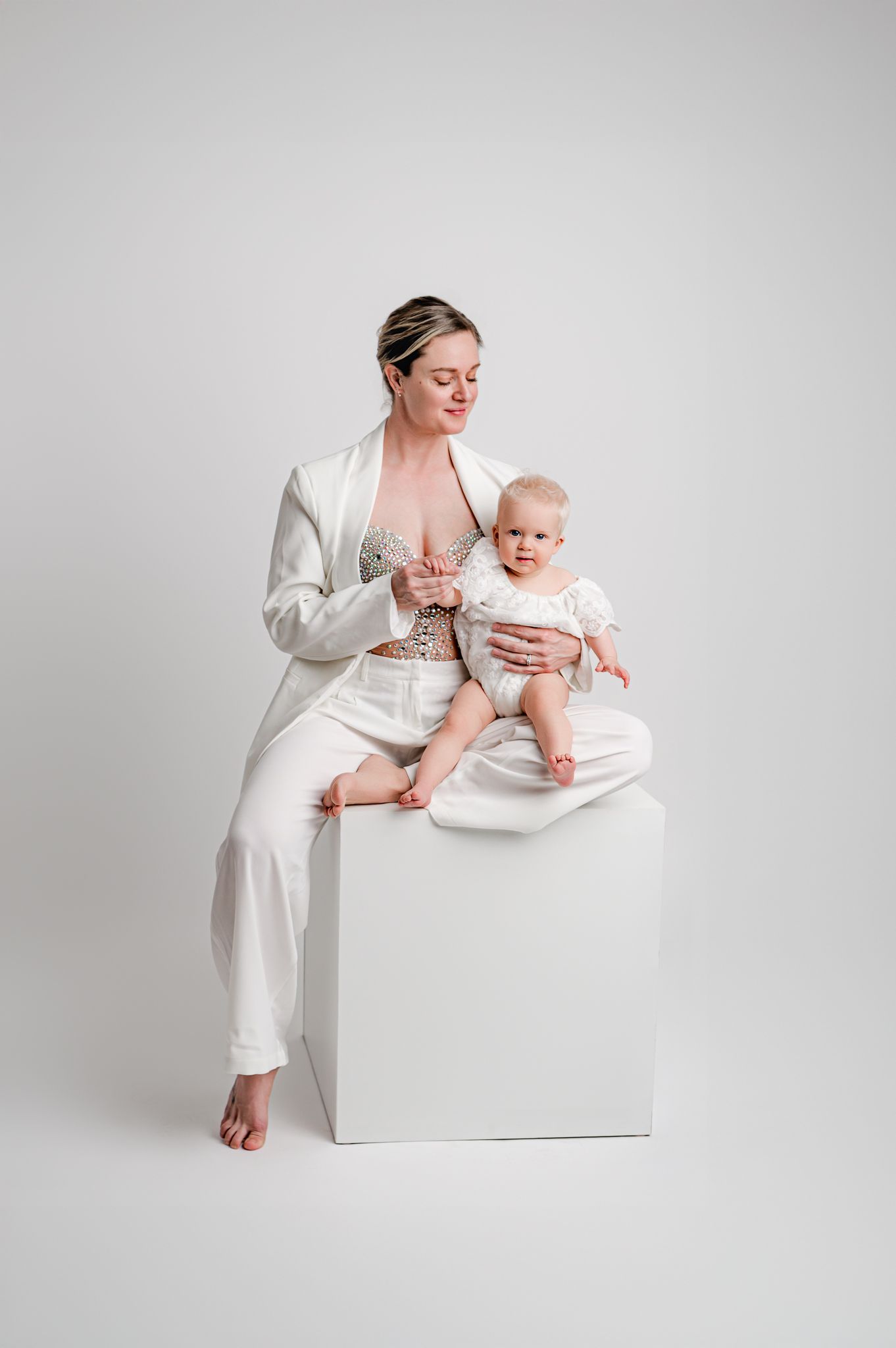 A minimalist studio portrait series showing tender moments between parent and baby in white outfits against light backdrop.