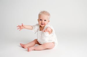 A baby in white clothing lies on a white background in various poses during a professional photo session.