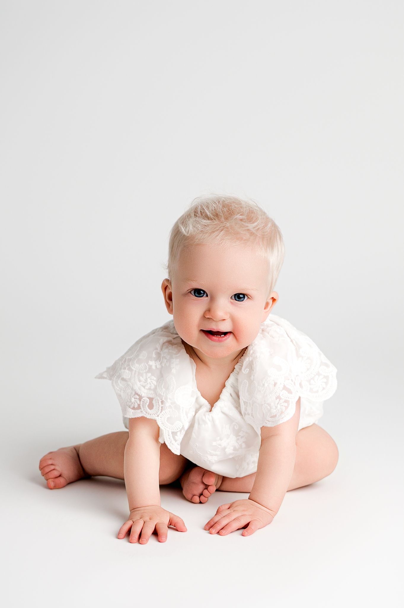 A happy baby in white lace outfit crawls and poses on white background in a series of three connected photos.