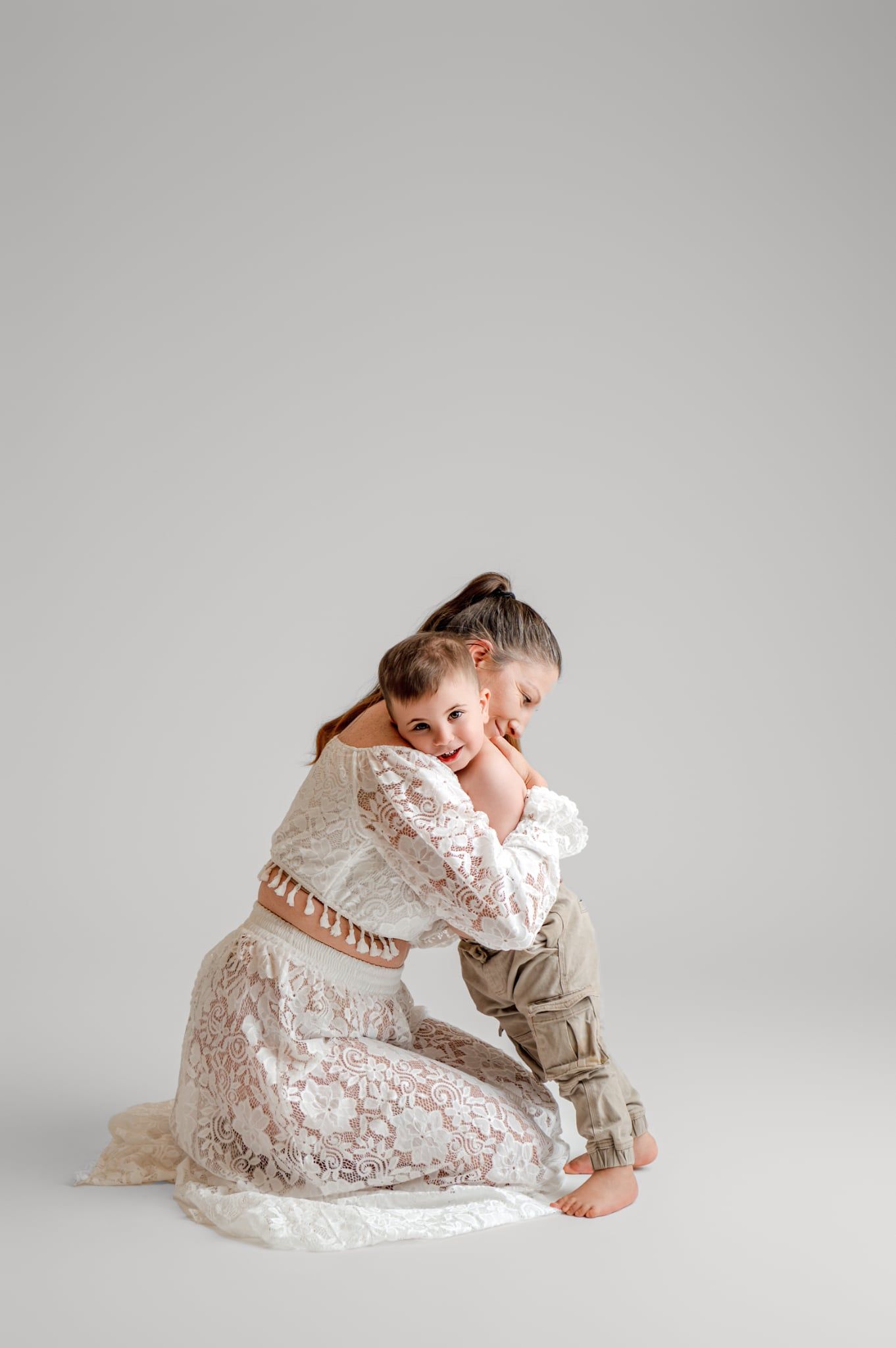 A series of artistic maternity portraits showing a pregnant woman in white lace dress against a light gray background.