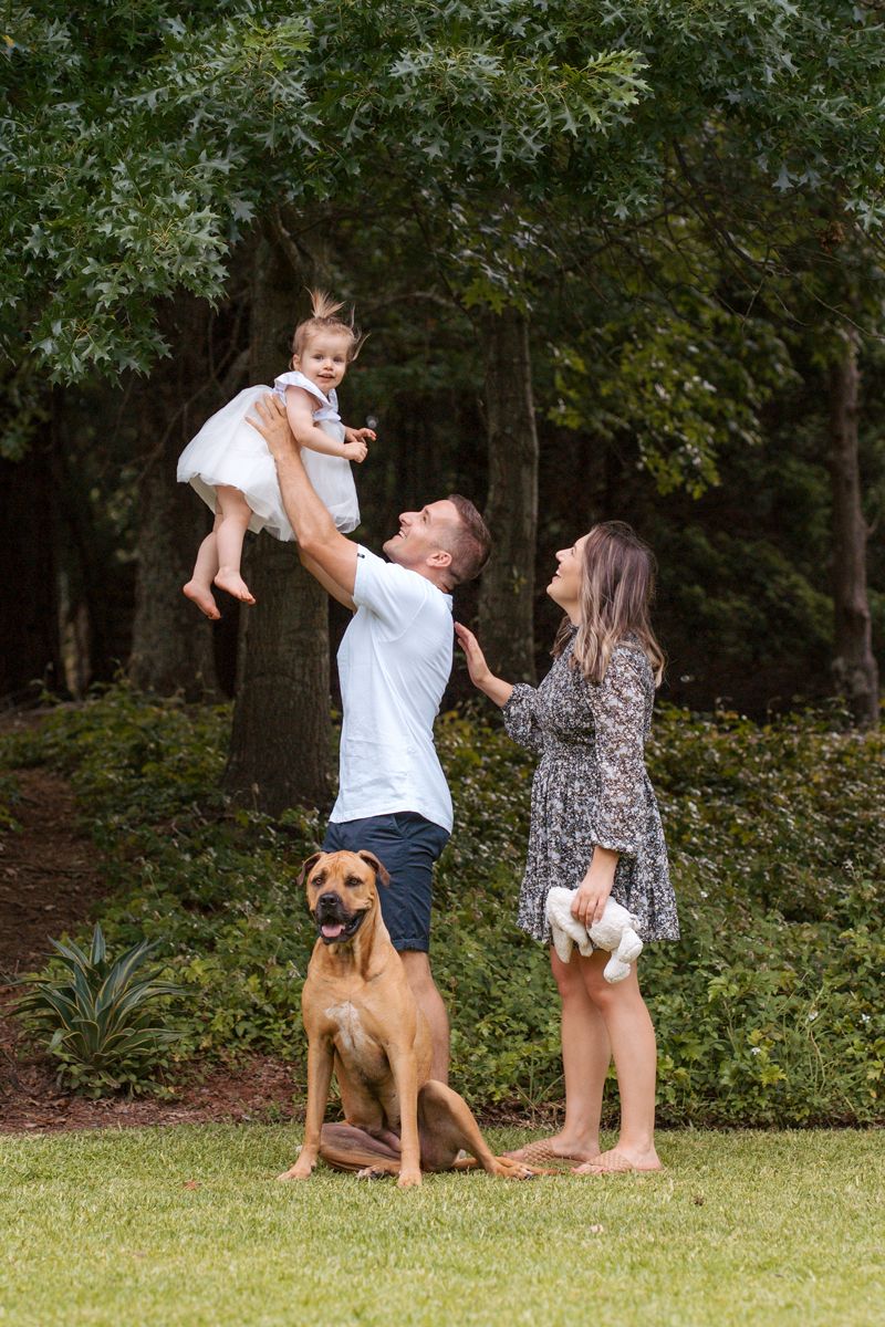 Family plays together in a backyard with their brown dog on a sunny day in a wooded setting during a family photoshoot with a dog in Sydney