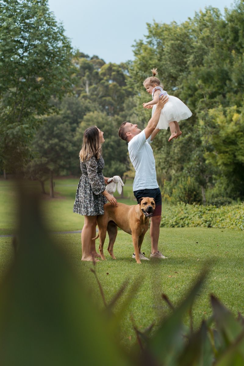 Family enjoying outdoor time together with their brown dog in a lush green park setting during a photoshoot in Sydney