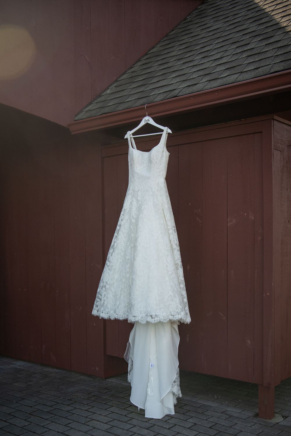 Full-length view of white lace wedding dress hanging outside against brown building.