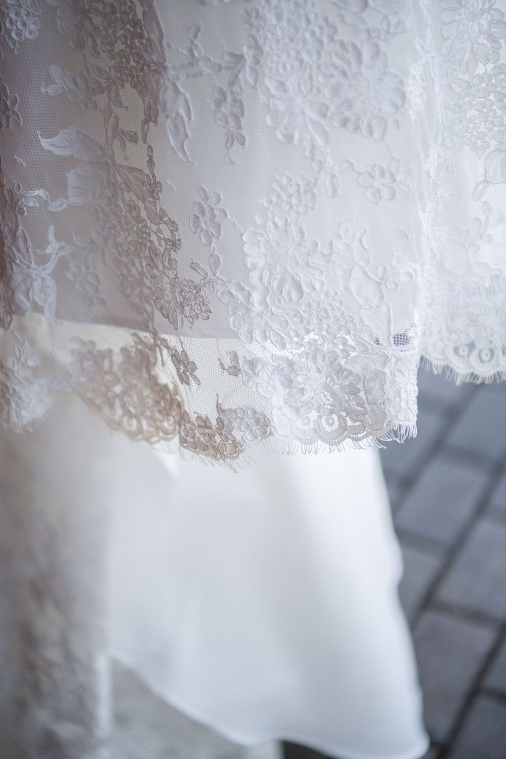 Close-up of delicate lace trim and fabric details on white wedding dress hem.