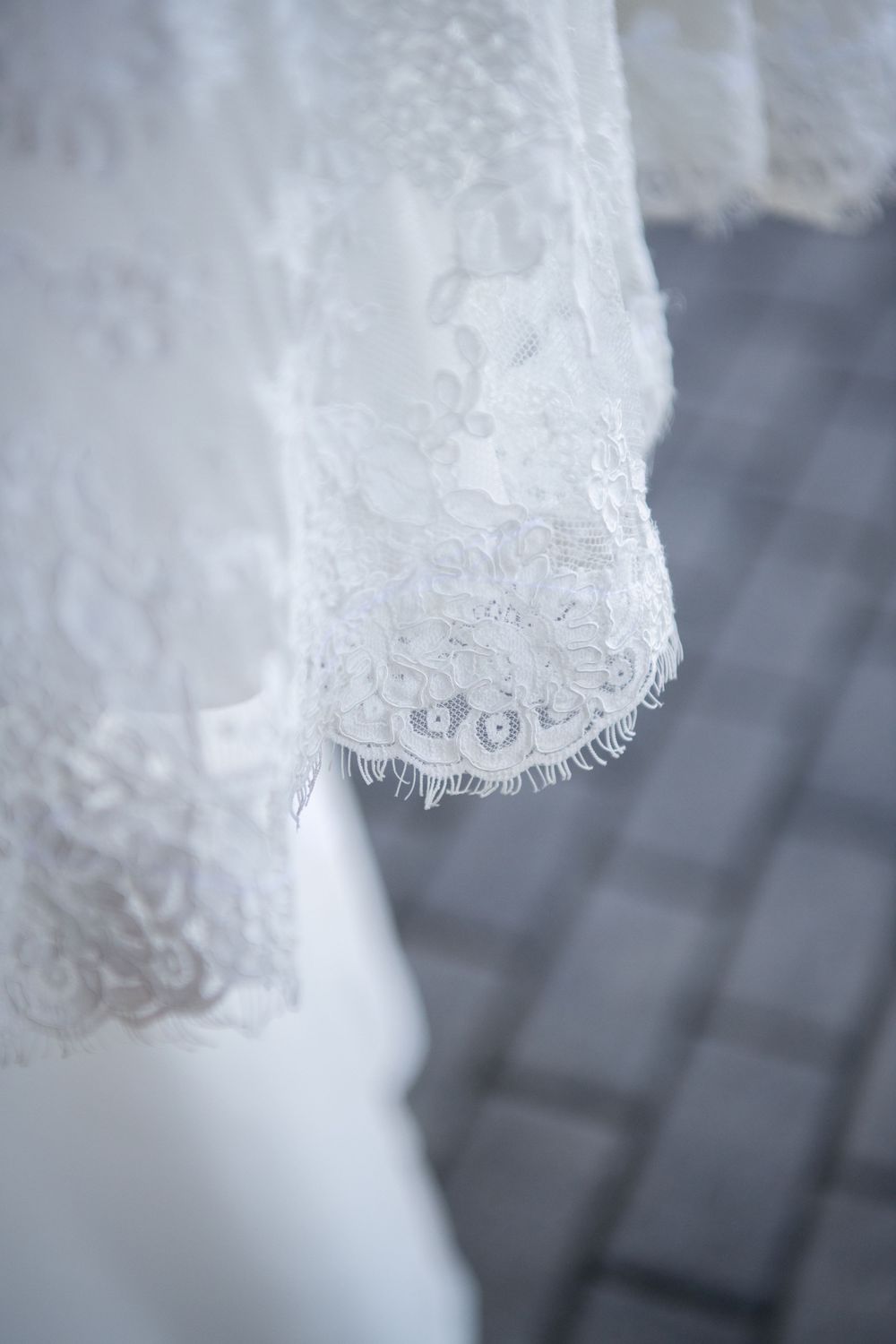Detailed macro shot of wedding dress lace pattern and hemline against dark background.