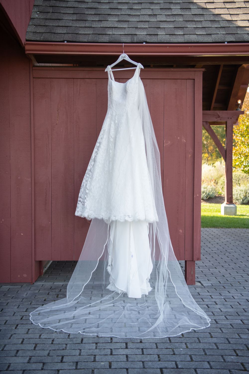 Elegant white wedding dress hanging against rustic red barn wall.