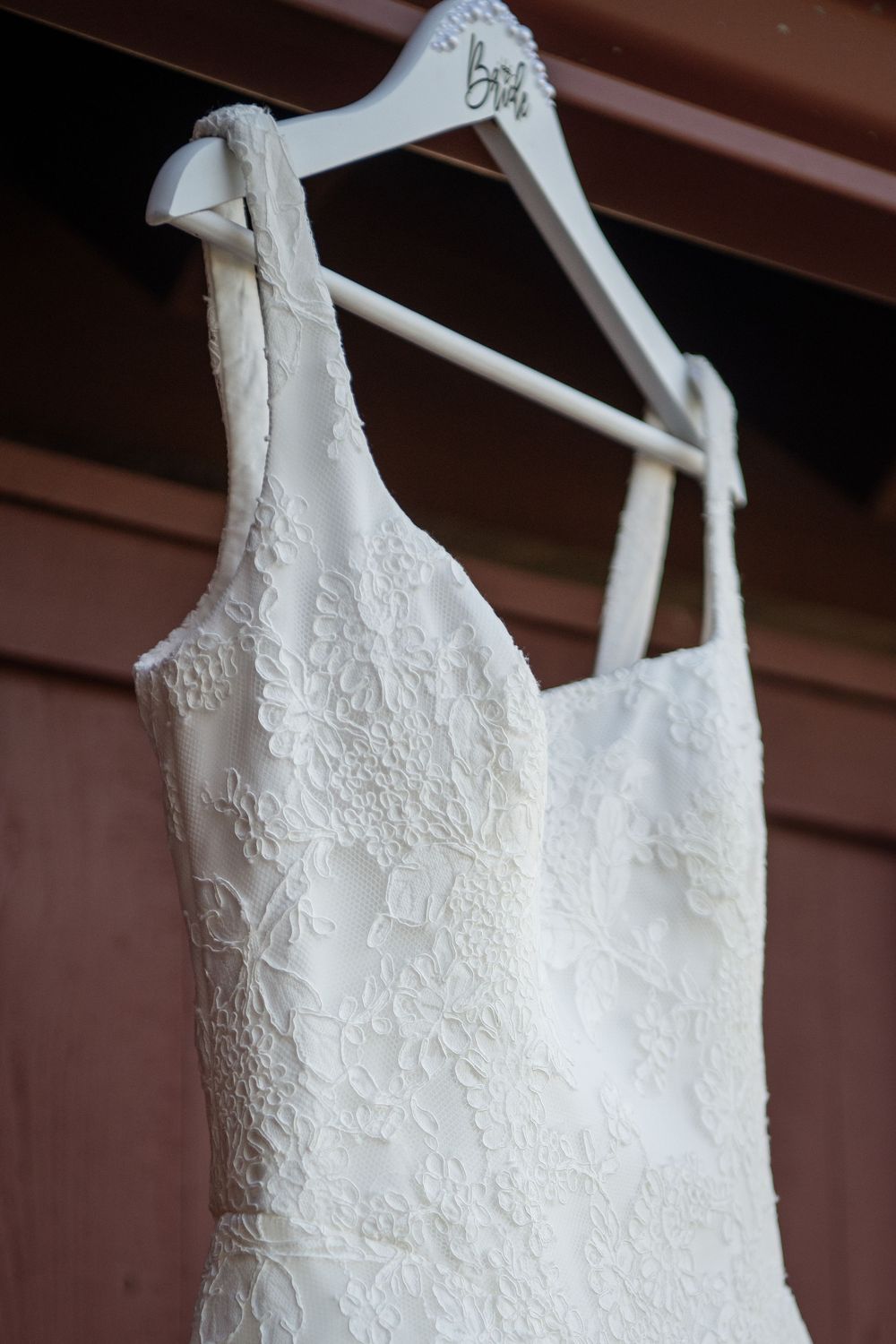 Close-up detail of delicate lace pattern on a white wedding dress hanging on display.