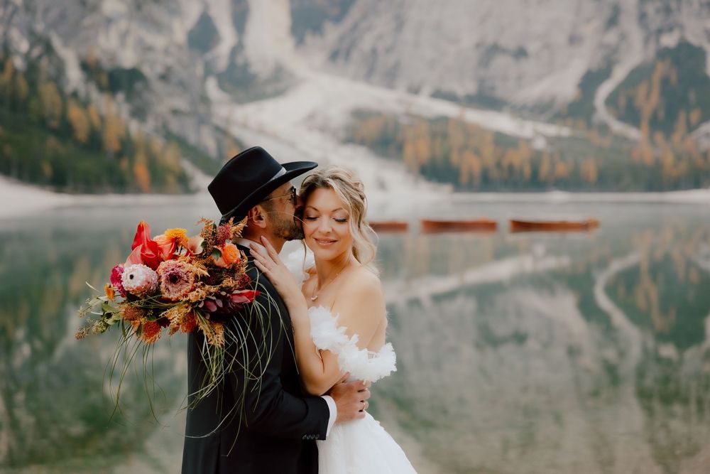 A couple embraces against a stunning mountain backdrop with snow-capped peaks and autumn foliage in the distance.