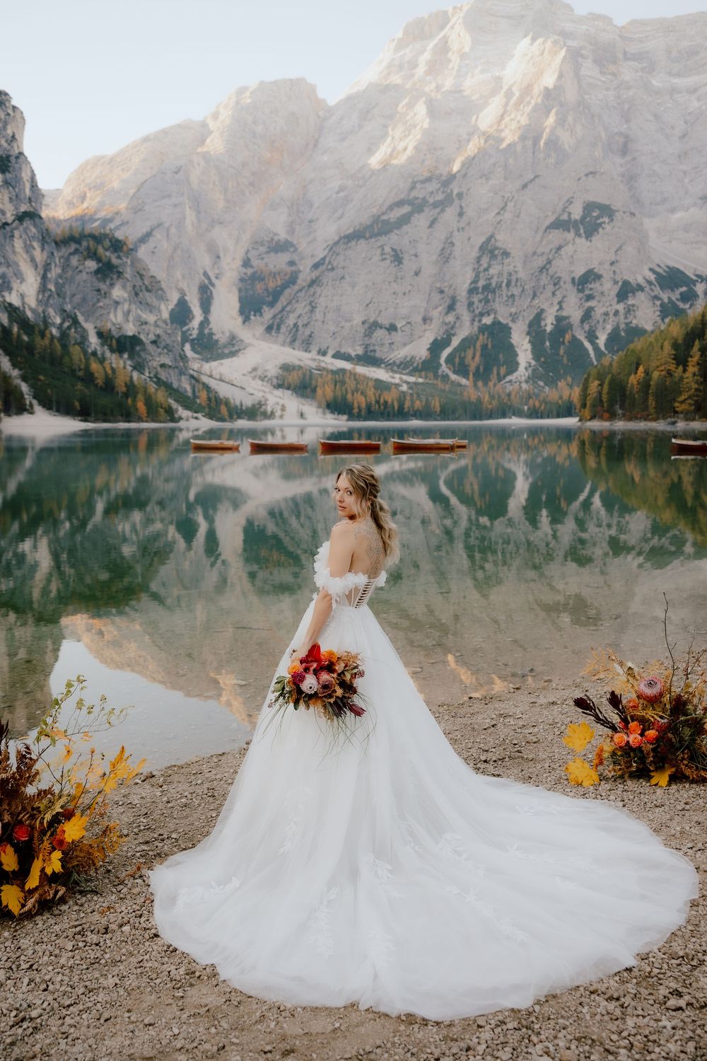 Stunning bridal portraits at Lake Braies in the Dolomites with dramatic mountain reflections and autumn florals.