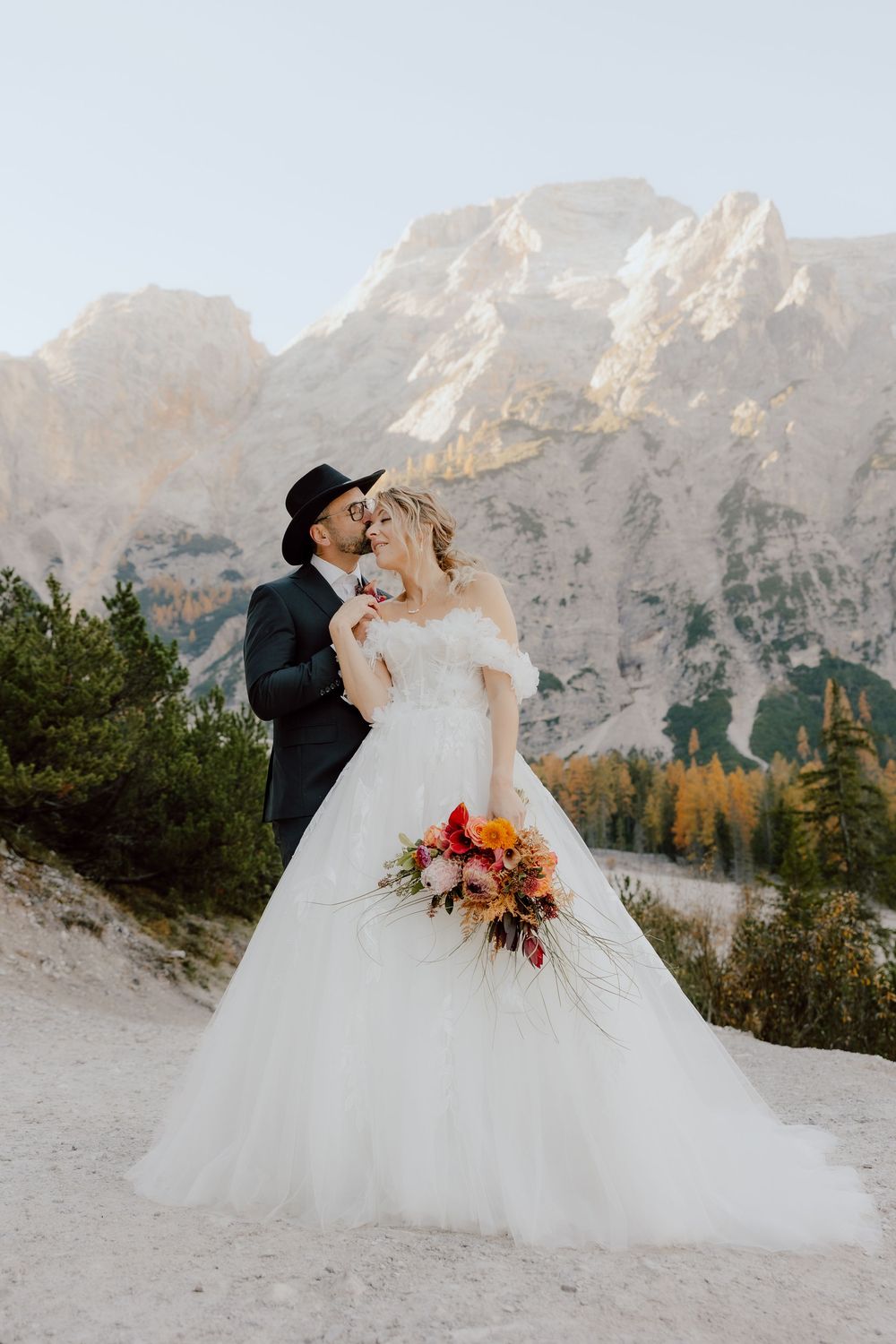 A wedding couple poses against majestic mountain peaks with fall foliage and a beautiful autumn bouquet.