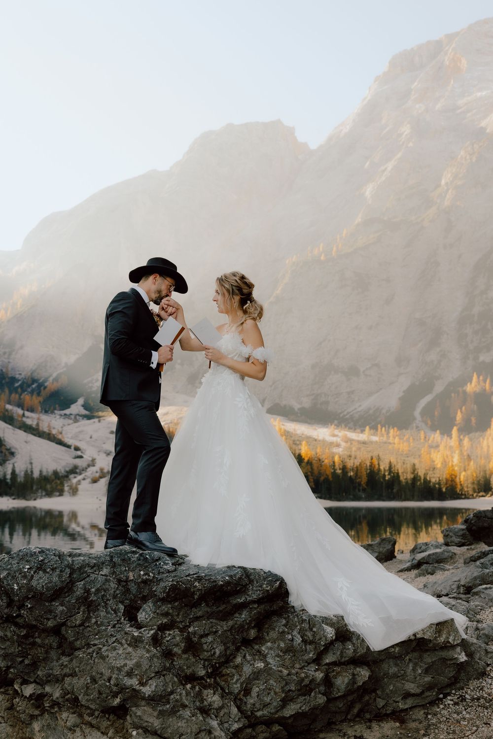 Newlyweds share romantic poses on rocky terrain with majestic mountain peaks in the background.