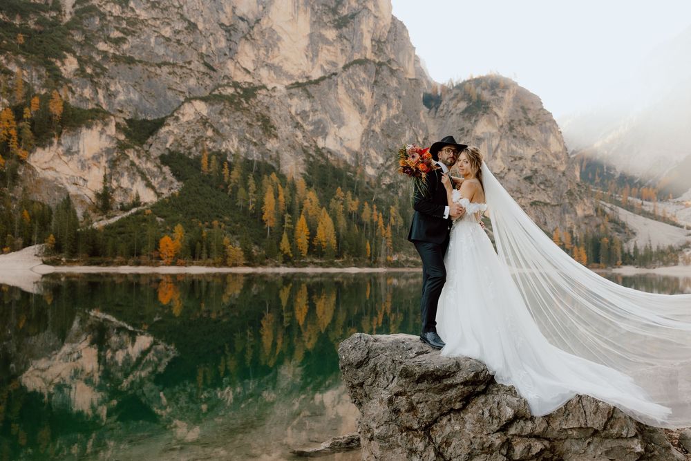 Couple embraces in front of majestic mountain landscape at Lago di Braies in the Dolomites during sunset.