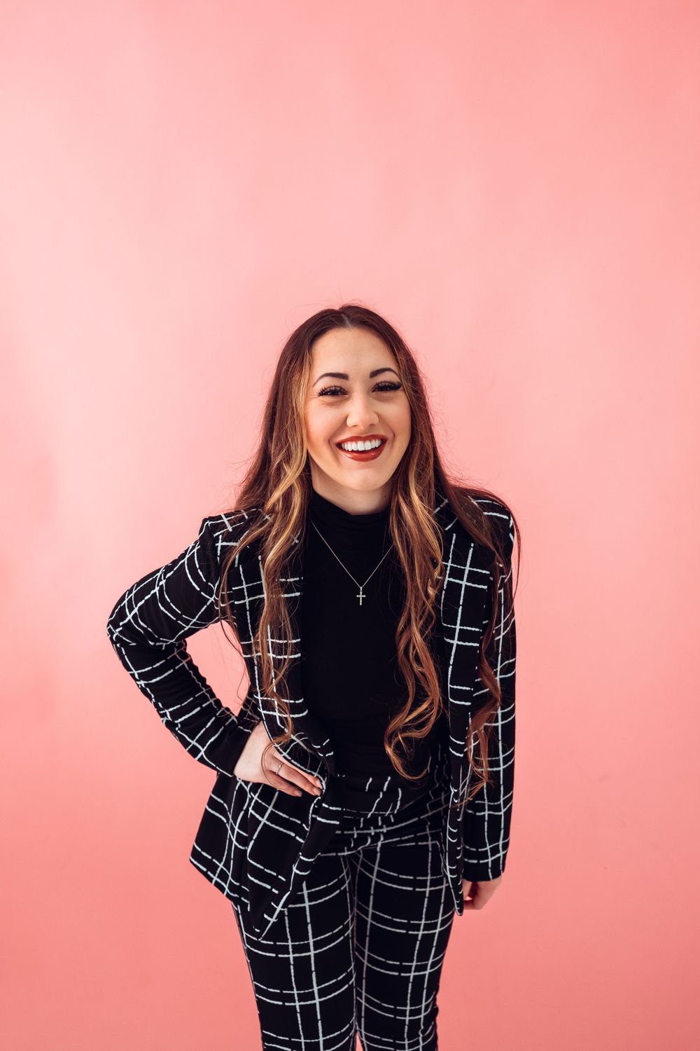 Professional wearing a stylish black and white plaid pantsuit poses against a pink background.