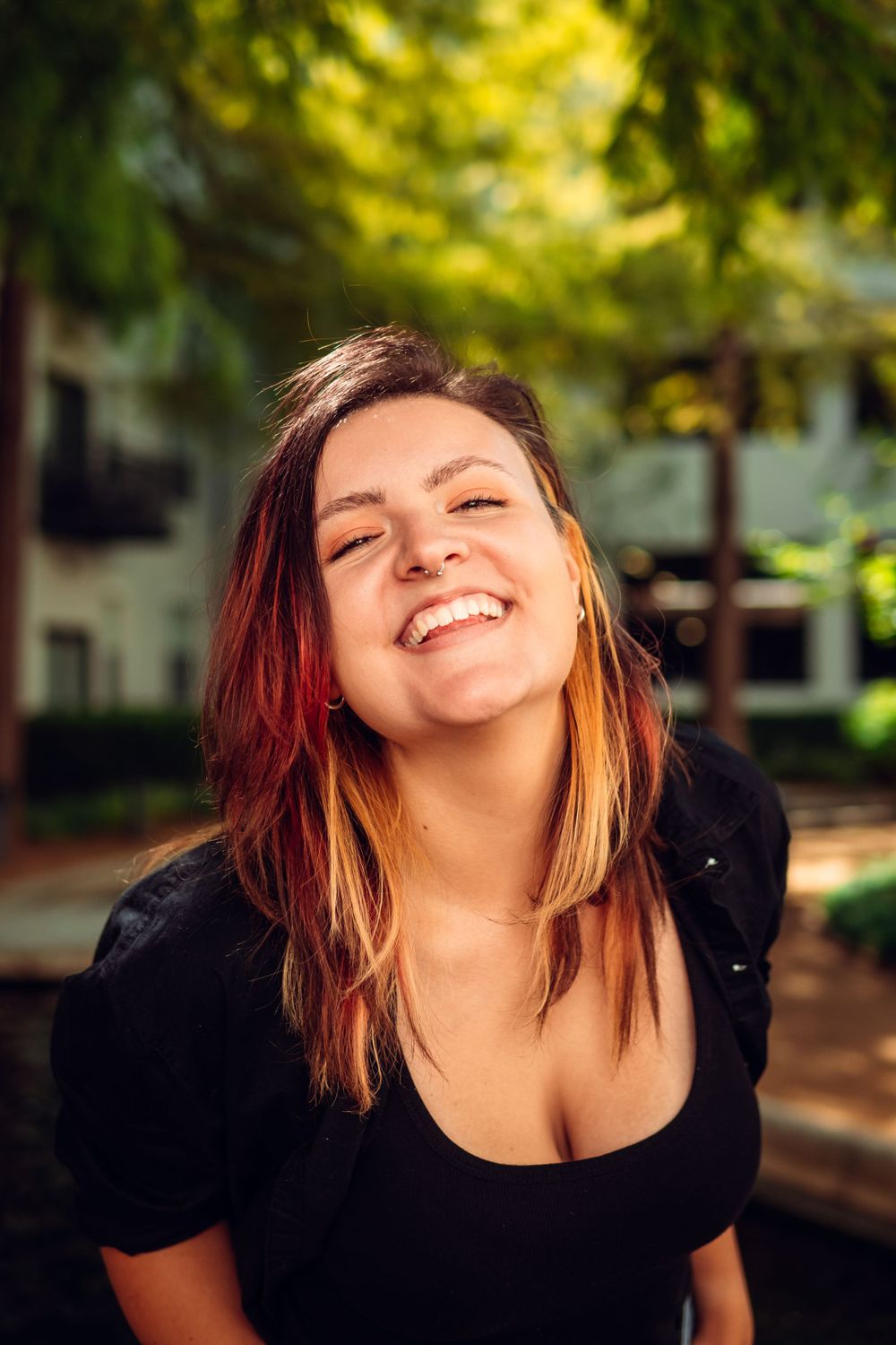 Woman with red-tinted hair smiling and laughing in outdoor setting with trees.